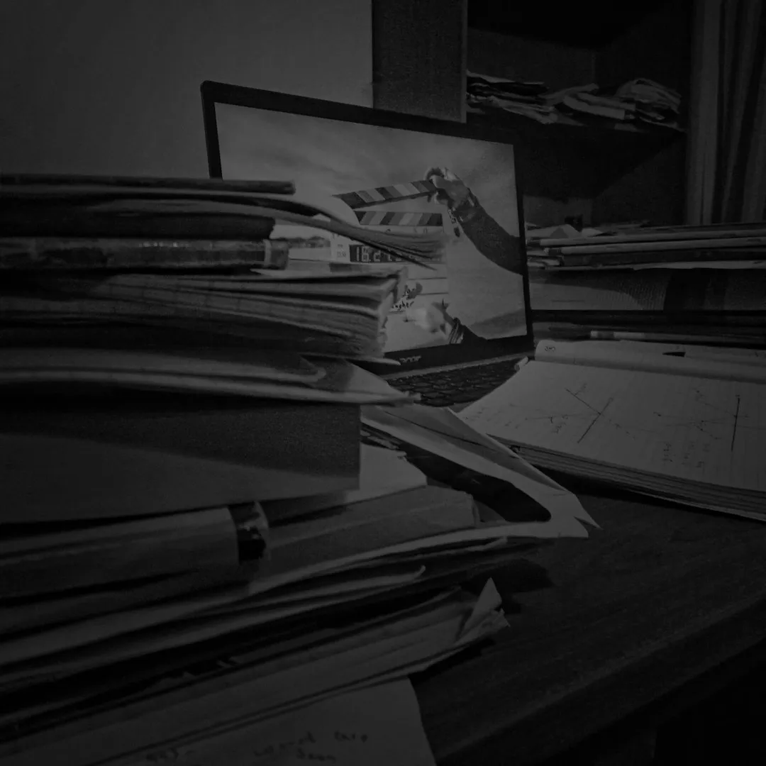 Чорно-біле зображення показує робочий стіл, заставлений великою кількістю паперових документів та па