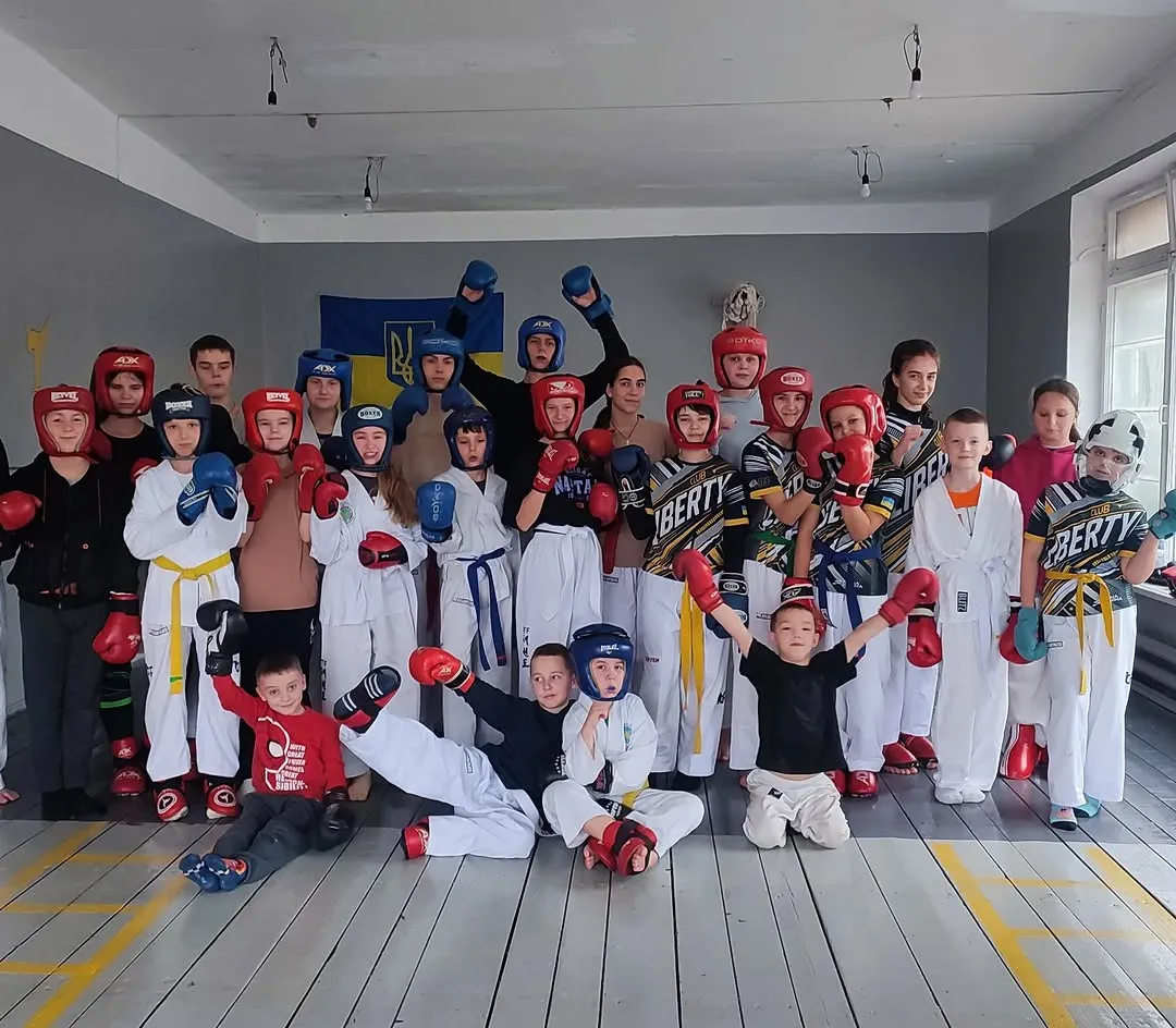 Групове фото дітей та тренера після тренування — всі в захисному спорядженні, руки вгору