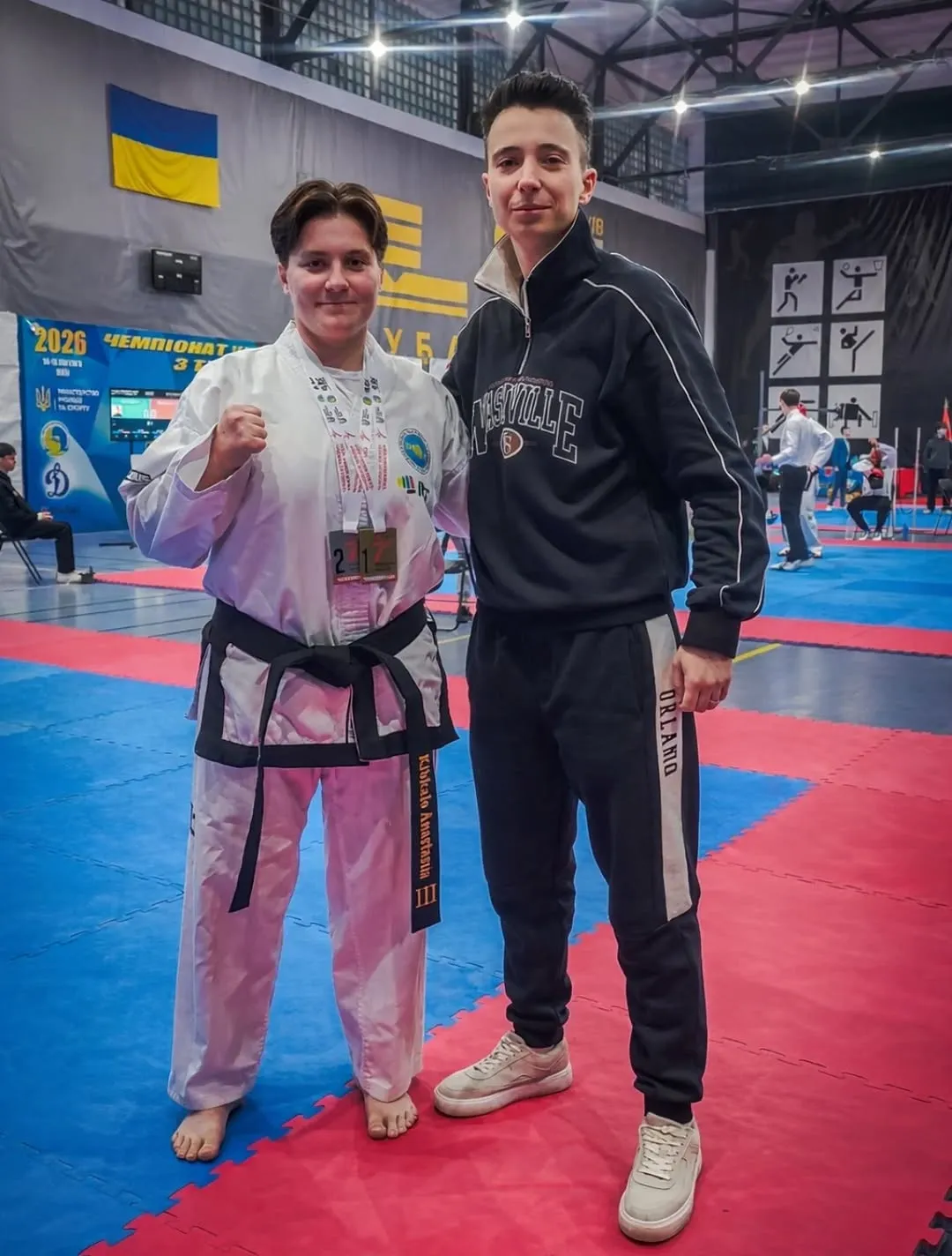 Тренер Анастасія Кібкало у білому кімоно з чорним поясом біля прапору України