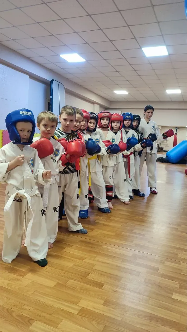 Діти в добоках з захисними шоломами вишикувалися для тренування в залі Liberty Club