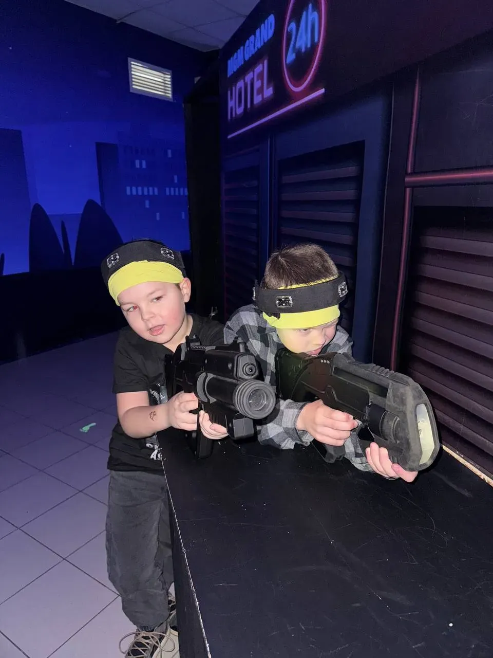 Двоє дітей з лазертаг обладнанням в темному приміщенні з неоновими вивісками