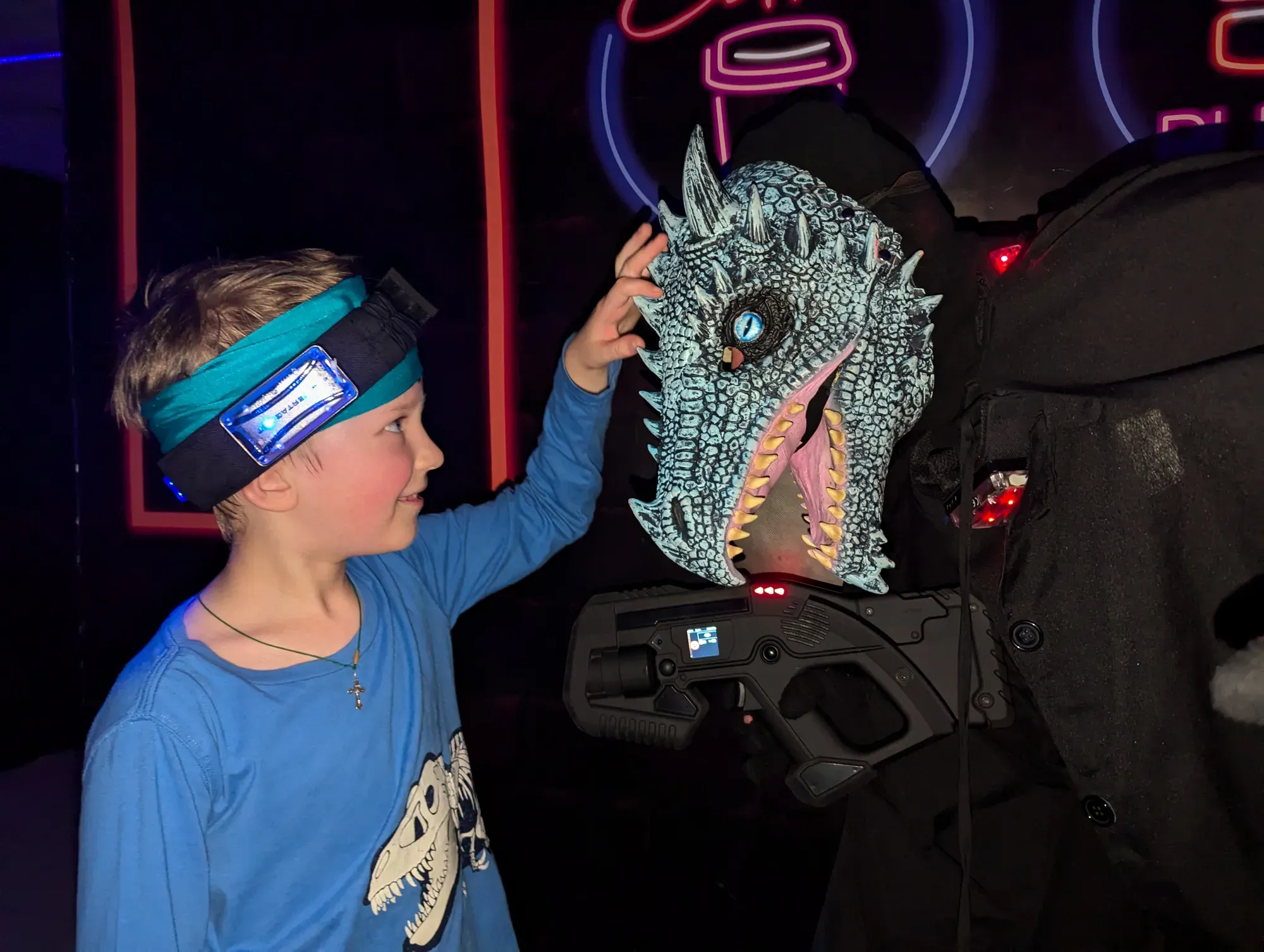 Дитина з маскою дракона та лазертаг зброєю в неоновому освітленні