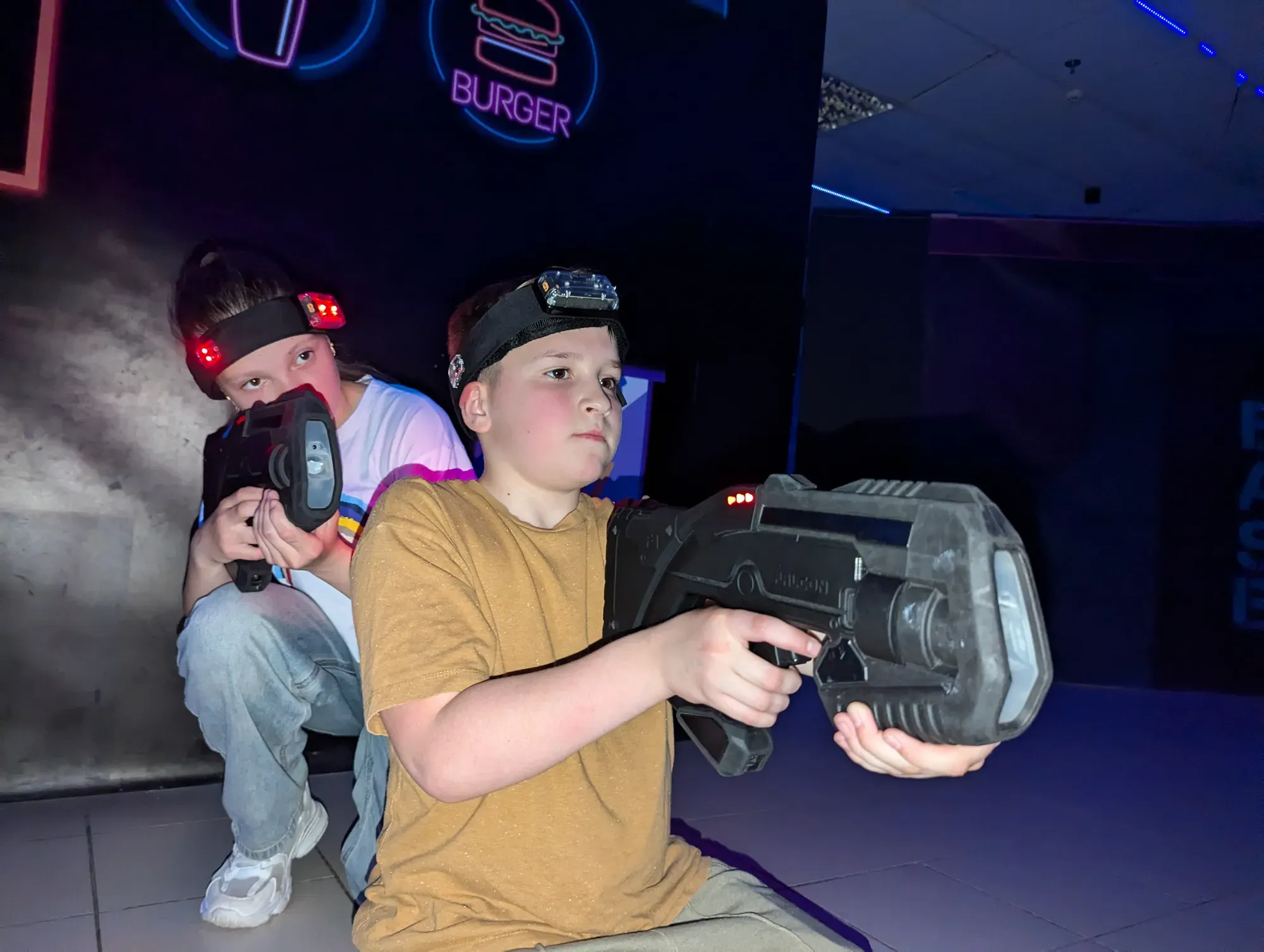 Хлопчик у жовтій футболці з лазертаг зброєю на неоновій арені