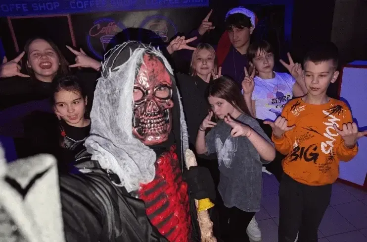 Діти з персонажем у масці на тлі фіолетового освітлення