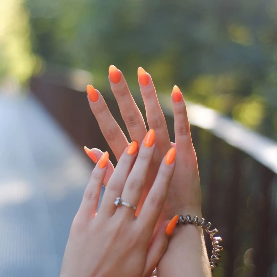 Яскравий кораловий манікюр на фоні зелені