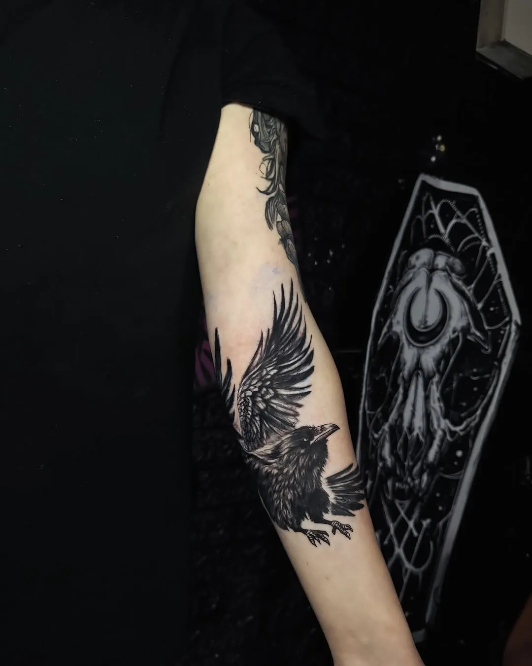 Тату ворона з детально прорисованим пір'ям на передпліччі